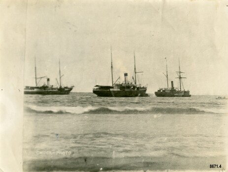Black and white photograph of three steamers at anchor in a bay. A small rowing boat with crew is on the right.