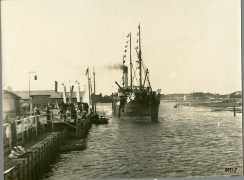 A steam ship with decorative flags is arriving at a pier