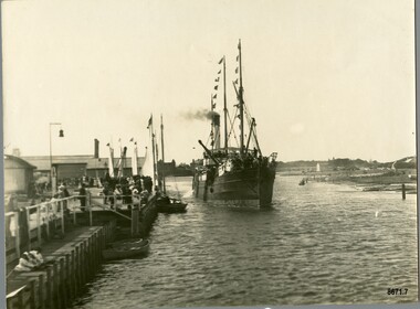 A steam ship with decorative flags is arriving at a pier