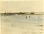 Colour tinted photograph of swimmers in front of a breakwater. A steamer is in the background. 