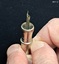 A two-piece round metal cigar piercer with a hollow spike in the middle of the base and a metal protective top.