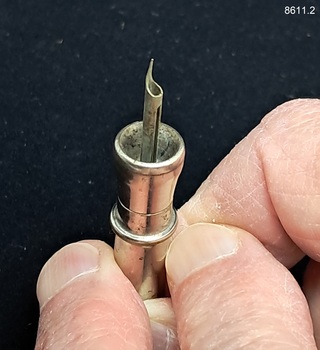 A two-piece round metal cigar piercer with a hollow spike in the middle of the base and a metal protective top.