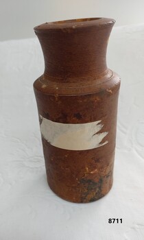Brown stoneware ink bottle with straight sides and remnant of tape on one side