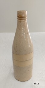 A beige stoneware bottle with two pieces of tape on one side