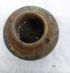 Cylindrical brass fitting with round 2 cm high threaded shank, rusted washer and a 2 cm wide flange above an octangular, flat cap.