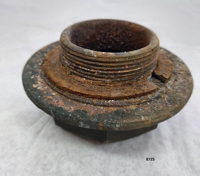Cylindrical brass fitting with round 2 cm high threaded shank, rusted washer and a 2 cm wide flange above an octangular, flat cap.