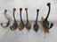 Six brass coat hooks - each with two hooks and four screw holes. One hook is attached to some wood.