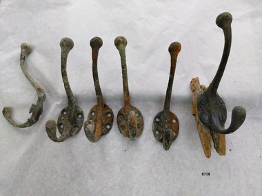 Six brass coat hooks - each with two hooks and four screw holes. One hook is attached to some wood.