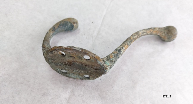 Brass coat hook with two prongs, four screw holes and verdigris patina.