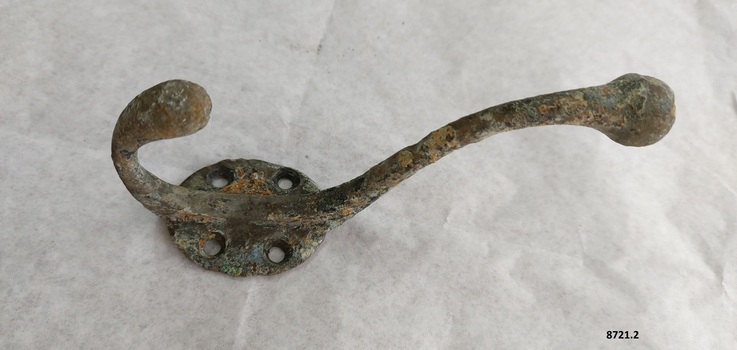 Brass coat hook with two prongs, four screw holes and verdigris patina.