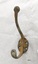 Metal coat hook with two prongs and four screw holes with a surface showing rust and corrosion.