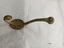 Brass coat hook with two prongs and four screw holes with a surface showing extensive green and brown oxidation.