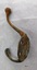 Brass coat hook with two prongs and four screw holes with a surface showing extensive green and brown oxidation.
