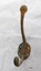 Brass coat hook with two prongs and four screw holes with a surface showing extensive green and brown oxidation.