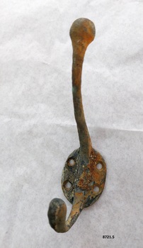 Brass coat hook with two prongs and four screw holes with a surface showing extensive green and brown oxidation.