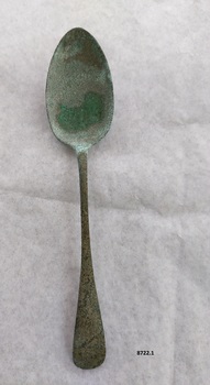 Front of silver tablespoon with green patina on base of "bowl" and neck of spoon.