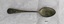 Front of teaspoon with rounded handle and small amount of tarnish and green patina.