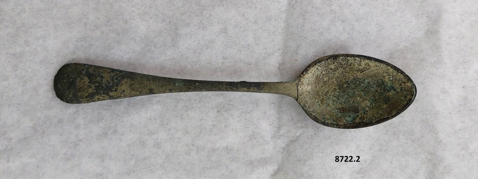 Front of teaspoon with rounded handle and small amount of tarnish and green patina.