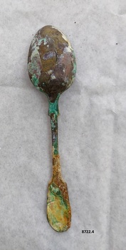 Back of dessert spoon, with fiddle back handle. Has green, purple and brown tarnish and corrosion.