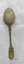 Back of dessert spoon with fiddle back handle. The thin metal has several small holes and is slightly encrusted with green and brown tarnish.