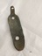 L shaped metal plate with one long, concave side (with two formed holes) and a narrow, short vertical arm with one hole. The inner side has a coating of green verdigris.