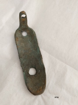 L shaped metal plate with one long, concave side (with two formed holes) and a narrow, short vertical arm with one hole. The inner side has a coating of green verdigris.