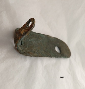 The narrow short outer side of an L shaped metal plate with one made hole showing a coating of green verdigris and a flaking layer of rust.