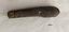 Pocket knife with metal top showing some corrosion and a brown wooden handle. 