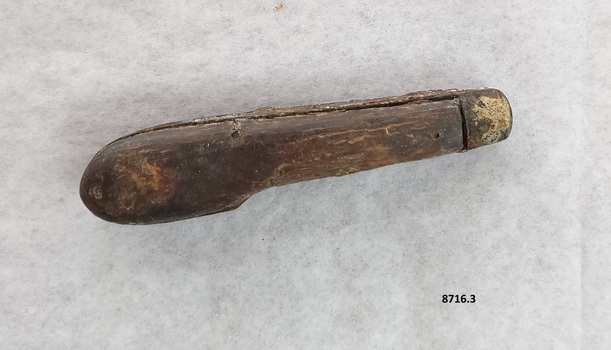 Side of pocket knife with brown wooden handle and metal cap showing some corrosion.