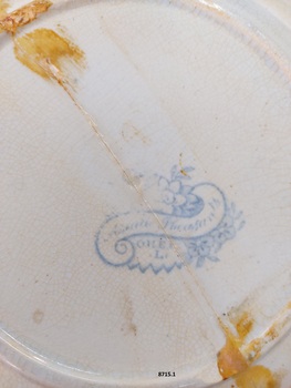 Blue maker's stamp on bottom of dinner plate featuring floral design with scroll and writing.