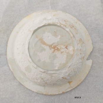View of the underneath of plate 8727.3 showing the missing chip and the blotchy, pitted surface where the glaze is missing.