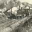 A steam train moves under a bridge