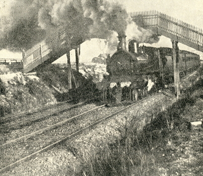 A steam train moves under a bridge