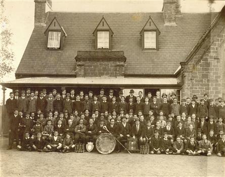 A number of teachers and students sit in front of a school