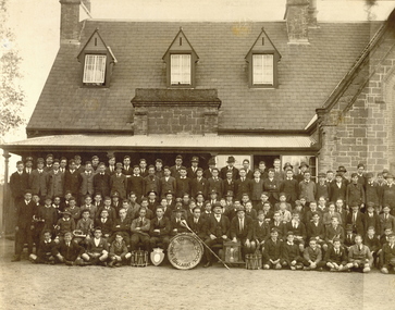 A number of teachers and students sit in front of a school