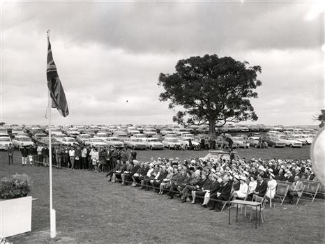 A seated audience, with cars in the background
