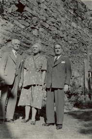 Photograph - Black and White, Frank Wright and two others in front of a large stone wall, 1950s - 1960s?