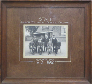 8 men in front of a bluestone school