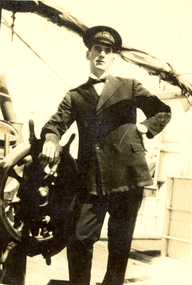 Photograph - Black and White, Frank Wright stands beside a ships wheel