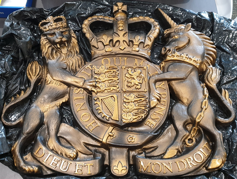 A gold coat of arms featuring a lion, unicorn and crown