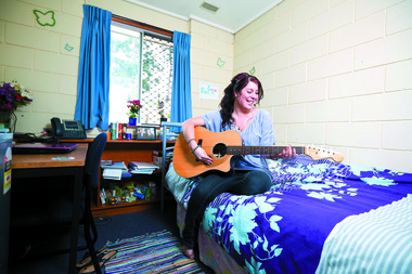 A woman plays a guitar on a bed