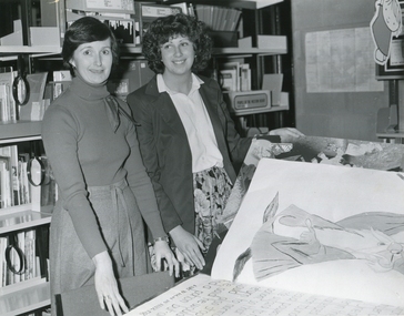 Two women look at a large book