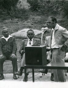 Four men, one stands at a microphone