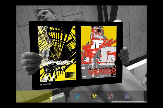 Black and white photograph of student, viewed from below holding a coloured presentation card of their work: two movie posters
