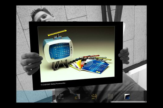 Black and white photograph of student, viewed from below holding a coloured presentation card of their work: three dimensional TV packaging and calendar inserts