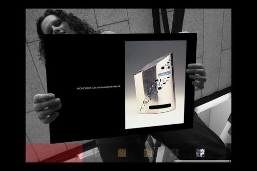 Black and white photograph of student, viewed from below holding a coloured presentation card of their work: silver metallic money box tin with applied graphics