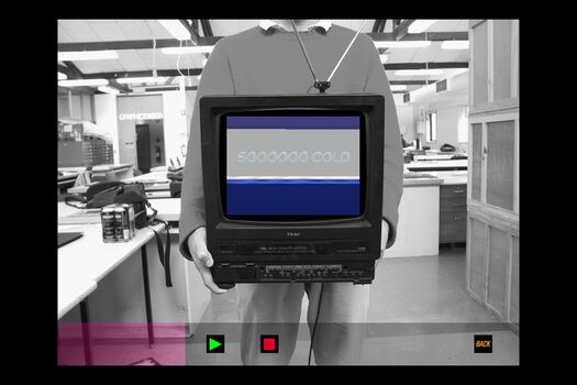 Black and white photograph of student in graphic design studio holding old television displaying a coloured animation