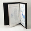 Opened black textured binder reveals plastic sleeves, holding student postcards.