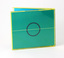 Blue paper sleeve housed in yellow plastic case (so printed item appears teal coloured). Small white text passes across open blue circle.