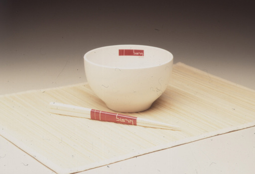 Image of white noodle bowl and chopsticks with red labels on bamboo placemat